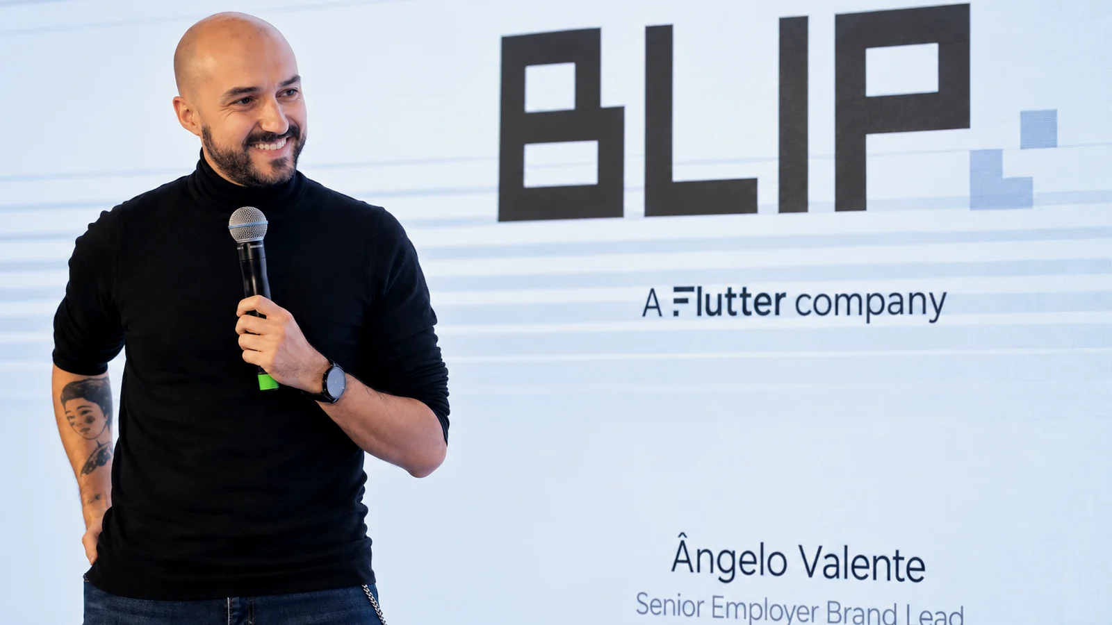 Ângelo Valente speaking on stage with a microphone at Rock in Rio, in front of a Blip title slide